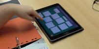 In der Tischmitte Liegt ein i-Pad auf dem Padlet geöffnet ist. In Padlet sind unterschiedliche Beiträge von Studierenden zu erkennen z.B. zu Funktionsgleichungen und Funktionsgraphen. Ein Studierender zeigt auf einen der Beiträge.